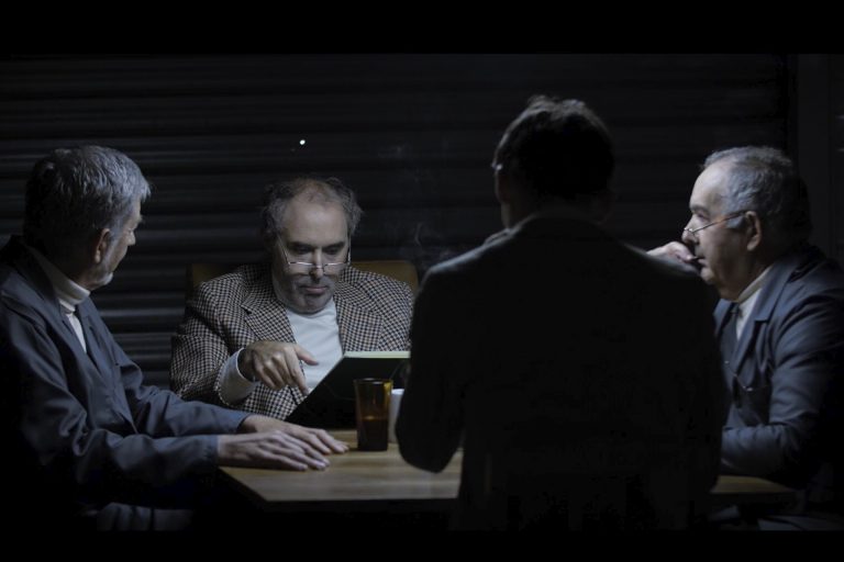 4 hommes autour d'une table dans une pièce sombre